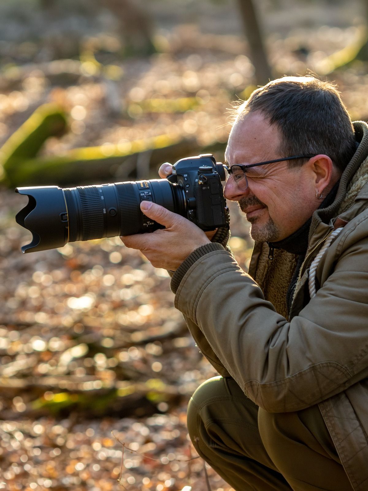 Olaf hockend bei der Arbeit im Winterwald, Kamera am Auge, Gegenlicht